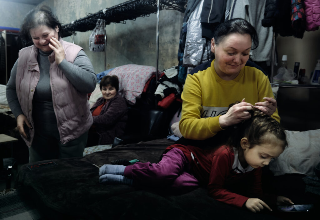 Donbas Fronltiner / Sofia is braiding the hair of her youngest daughter, Vila. Her friend Tanha is laughing on the left