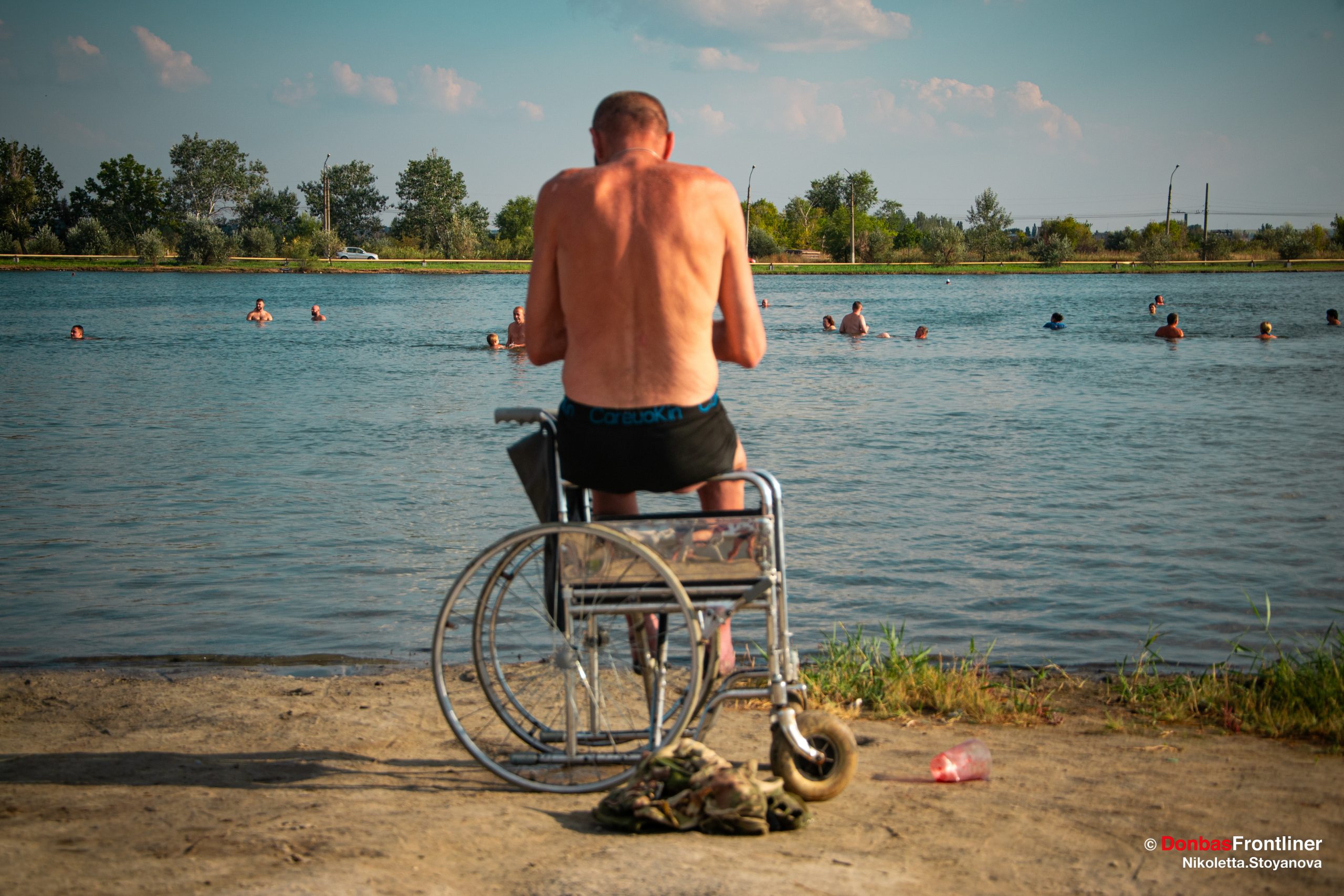Солдат з ампутованими ступнями внаслідок підриву на міні сидить в інвалідному візку і дивиться на людей в озері під Слов'янськом. Він, ймовірно, ніколи більше не зможе плавати. Вересень. Слов'янськ, Донецька область Ніколєтта Стоянова / Donbas Frontliner